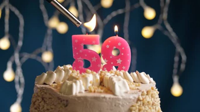 蓝色背景上有59号粉色蜡烛的生日蛋糕。蜡烛着火了。慢动作和特写视图