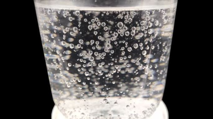 黑色背景上有水的玻璃中的气泡的宏观视频。气泡从玻璃底部升起。矿泉水与气体的特写。