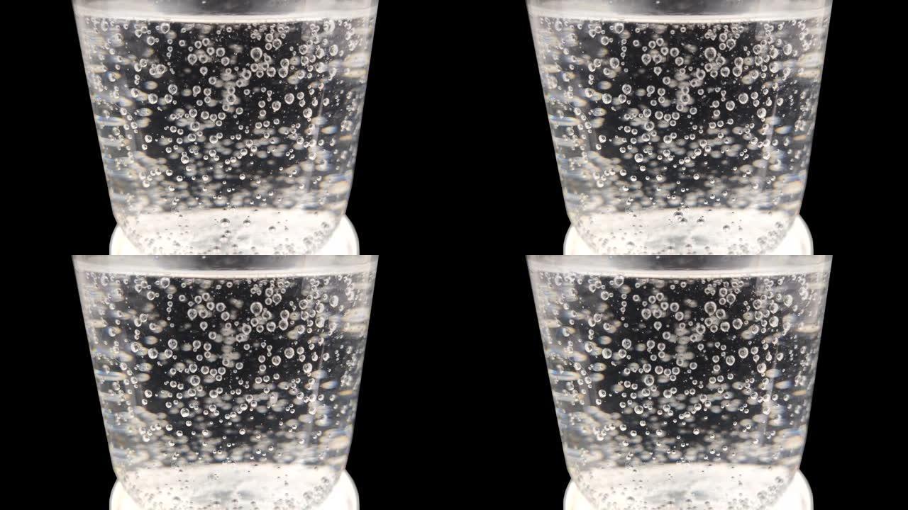 黑色背景上有水的玻璃中的气泡的宏观视频。气泡从玻璃底部升起。矿泉水与气体的特写。