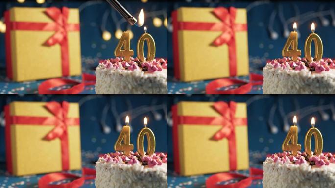 白色生日蛋糕40号点火器燃烧的金色蜡烛，蓝色背景带灯和用红丝带绑起来的礼物黄色盒子。特写