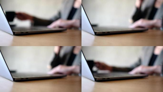 一名妇女触摸笔记本电脑触摸板并喝咖啡
