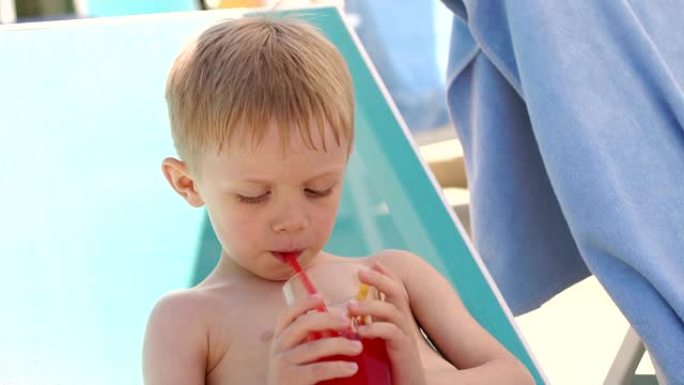 夏天，一个金发小男孩在游泳池边喝鸡尾酒的特写镜头。