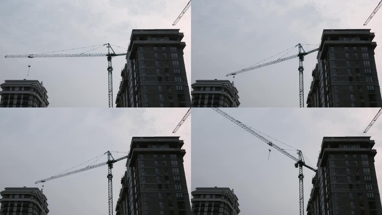 正在建造的摩天大楼，配有巨大的起重机。雨天在灰色多云的天空下在建筑工地上工作的起重机