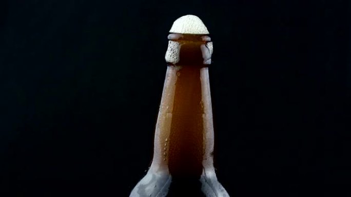 啤酒泡沫从雾状的瓶子里流下来。泡沫从一瓶黑啤酒中流下来。在黑暗的背景上特写一瓶啤酒。