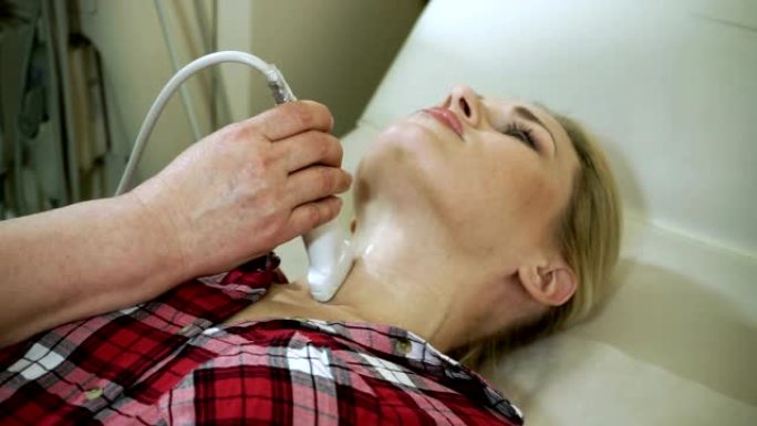 女医生使用超声波扫描仪检查妇女的甲状腺。高清