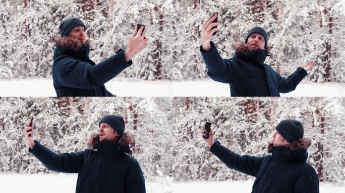 一位帅气的视频博主的肖像旅游男子在白雪皑皑的冬林中使用手机，自拍，视频会议，视频博主