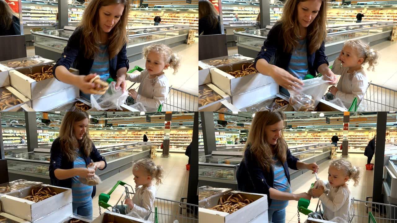 怀孕的母亲和蹒跚学步的女孩在购物市场采摘百吉饼