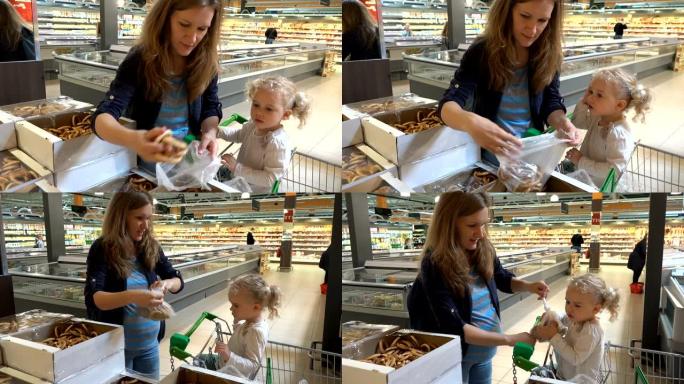 怀孕的母亲和蹒跚学步的女孩在购物市场采摘百吉饼