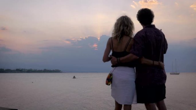 一对中年夫妇在海洋上看着日落时互相抱着