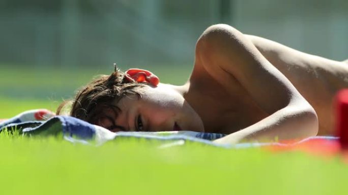 孩子躺在阳光下的草地上，小男孩在户外做白日梦