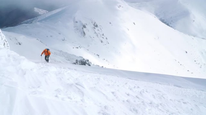 高登山者穿着鲜艳的橙色软壳夹克，用登山杖登上雪山山顶。4K UHD电视活跃人物概念镜头。