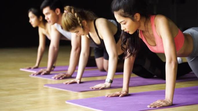 在健美操课上在瑜伽垫上做俯卧撑练习的亚洲男女团体。年轻的运动人士在健身房的地板上一起锻炼。