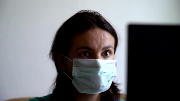 女人戴上面具，在笔记本电脑上阅读有关病毒的最新消息，看上去对一杯茶感到震惊和沮丧，有趣