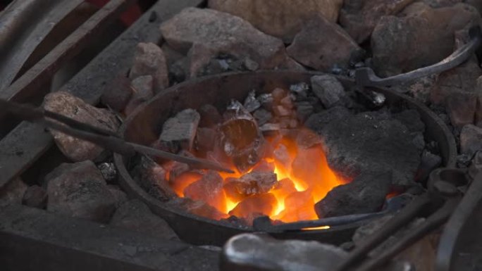 铁匠在锻造中工作。火在燃烧，金属在炉膛的煤中融化。锻铁。