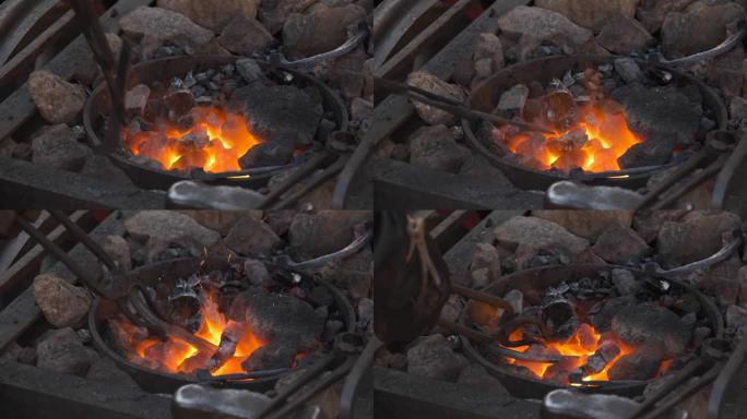 铁匠在锻造中工作。火在燃烧，金属在炉膛的煤中融化。锻铁。