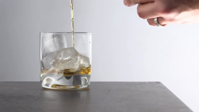 调酒师将陈年的金色威士忌倒入桌上有冰块的玻璃杯中。琥珀色酒精饮料，白色背景上有岩石
