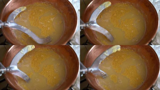 在铜大锅中煮沸黄色玉米粉并搅拌搅拌器的俯视图，传统意大利热菜的制备过程，在火炉上煮熟的美味玉米粥。意