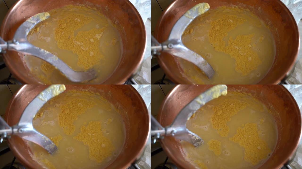 在铜大锅中煮沸黄色玉米粉并搅拌搅拌器的俯视图，传统意大利热菜的制备过程，在火炉上煮熟的美味玉米粥。意