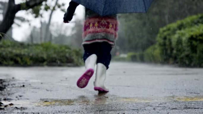 一个小女孩在水坑里跳伞的慢动作在雨中撑着伞