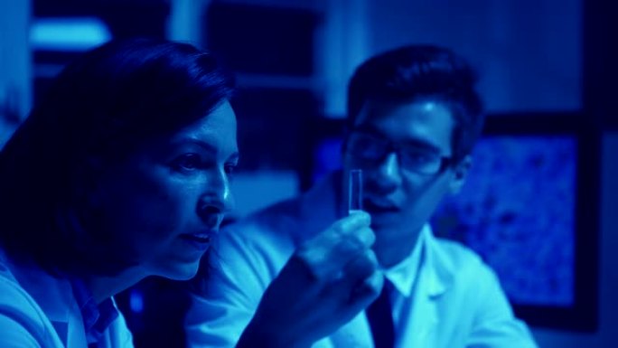 两名震惊的生物化学科学家的蓝色色调单色照片，男人和女人穿着实验室外套，仔细检查并讨论实验室试管中的液