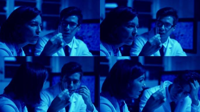 两名震惊的生物化学科学家的蓝色色调单色照片，男人和女人穿着实验室外套，仔细检查并讨论实验室试管中的液