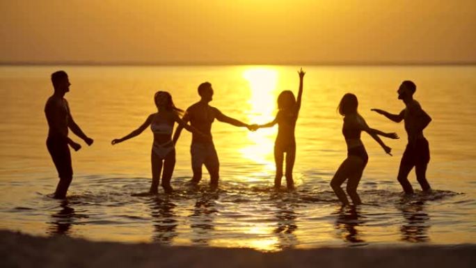 一群朋友在美丽的夕阳下玩到水里。慢动作