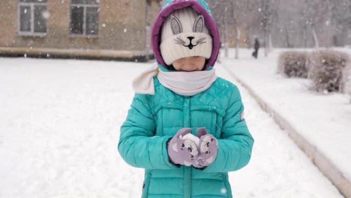 小女孩冬天放学回家，手里雕刻着一个雪球。