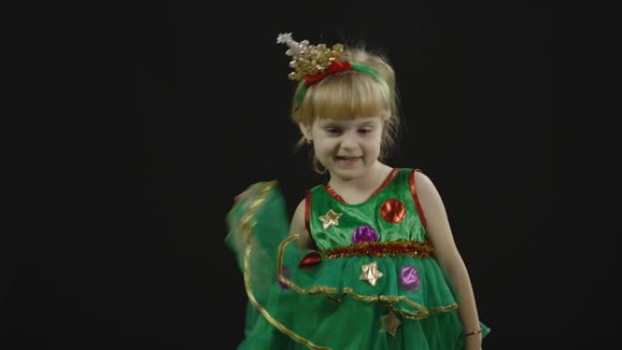 快乐美丽的小女孩，穿着圣诞树服装。做鬼脸，跳舞