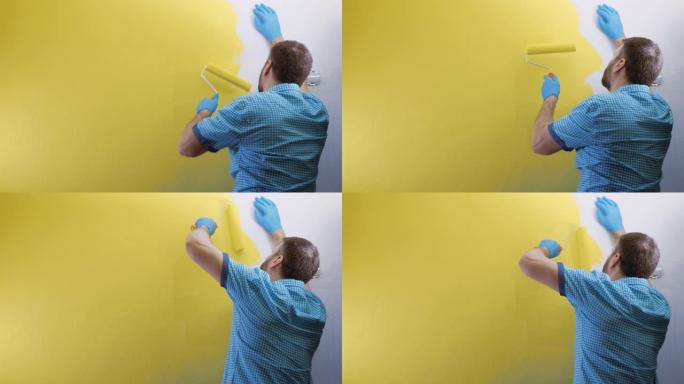 疲倦的人用黄色的左手用滚筒画白色的墙壁。他穿着格子蓝色衬衫和手套。慢动作和中等镜头
