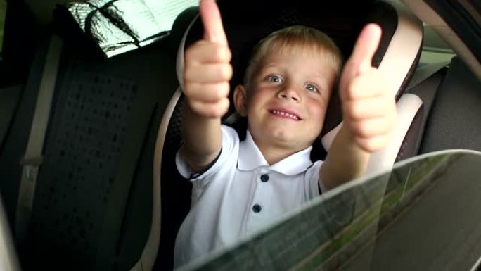 一个开朗的小男孩坐在棕色的儿童汽车安全座椅上，竖起大拇指。