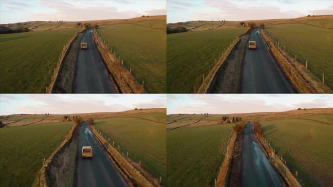 在美丽的日落时分，一辆车在后面有一只狗的车辆穿越英国乡村的农地时，航拍镜头