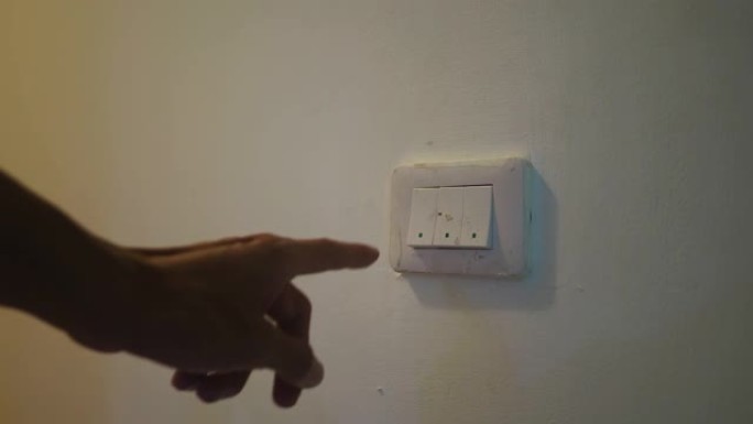 挂在墙上的灯泡在照明开关上用人的手关闭。