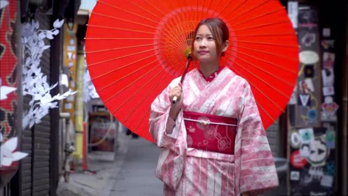 4k快乐年轻美丽的亚洲女子穿着传统的日本和服连衣裙，拿着红色纸伞微笑着走在街上，日本东京市新宿地区