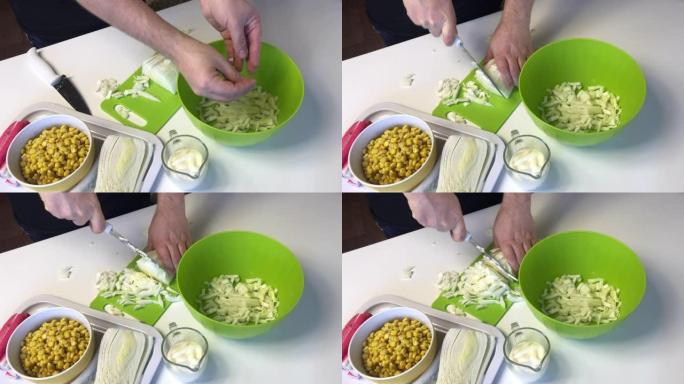 一个男人做北京白菜沙拉。用菜刀将白菜切成薄片，然后将其放入容器中。桌子旁边是其他配料。玉米、蟹棒和蛋