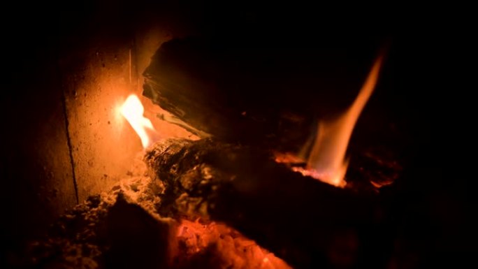 夜间在耐火玻璃后面的现代家用炉灶中，用煤昏暗燃烧的柴火的特写镜头。低调。摄像机转动时靠近火炉移动。环