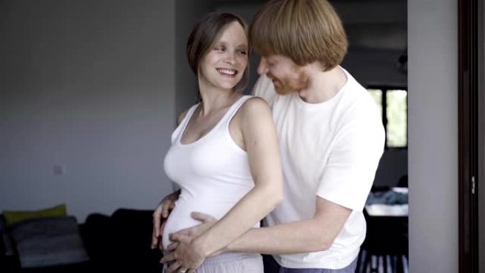 微笑的丈夫走路拥抱怀孕的妻子