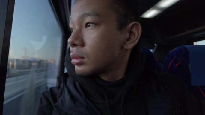 亚洲男子透过公共汽车窗户看。