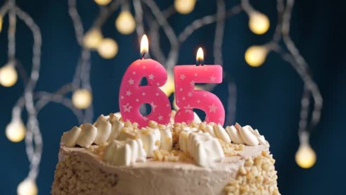 蓝色背景上有65号粉色蜡烛的生日蛋糕。蜡烛吹灭了。慢动作和特写视图