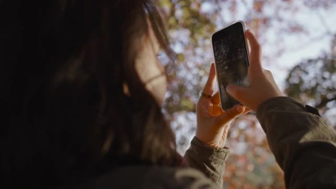 一名亚洲妇女站在公园，用手机拍摄全景照片。