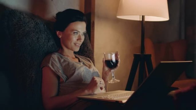 女人用笔记本喝红酒。女孩看带酒杯的笔记本电脑。