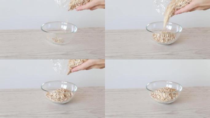燕麦薄片倒入木制背景的玻璃碗中