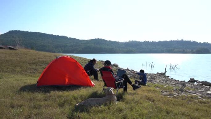 草地上的红色野营帐篷。湖岸上的母亲和儿子