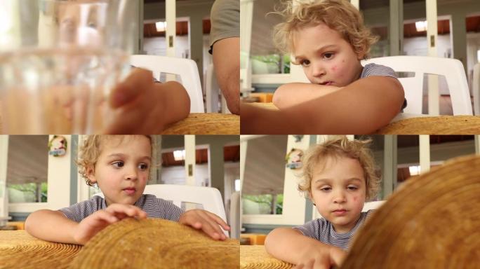 无聊的小男孩在午餐桌上玩玻璃和餐具