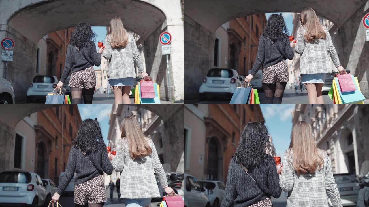 两名时装模特带着满满的购物袋和开胃酒鸡尾酒杯沿着市中心的街道行走的后视图。女孩谈论时尚和美丽，奢侈的