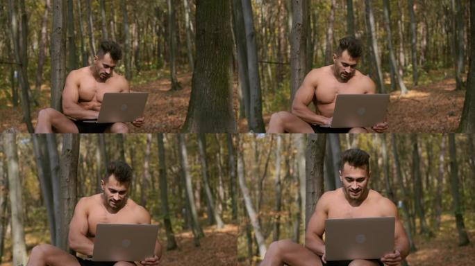 强壮的裸体躯干家伙坐在秋天的公园里，手里拿着笔记本电脑。