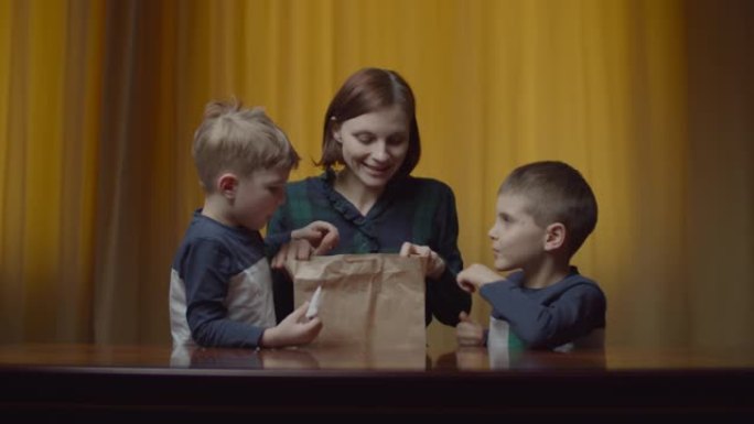 母亲带着两个孩子用午餐打开送货包装盒。快乐饥饿家庭闻食物送货袋。