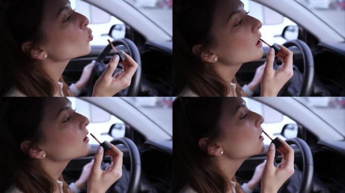 给保持汽车方向盘的高加索女孩涂唇彩。危险驾驶。车轮上的化妆