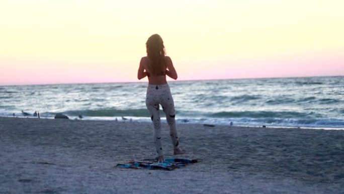 穿着紧身衣的年轻女子在海上海滩上练习瑜伽