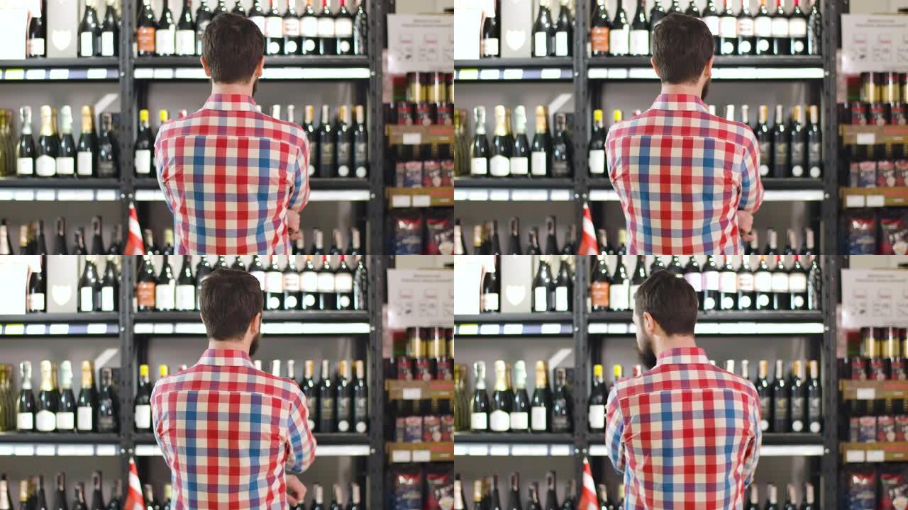 年轻的大胡子高加索人检查酒瓶架子的后视图。侍酒师在葡萄酒商店选择晚上最好的饮料。生活方式、消费主义、