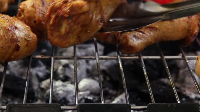 烧烤烤架上的烤鸡腿。烹饪过程。用铁钳翻转肉禽